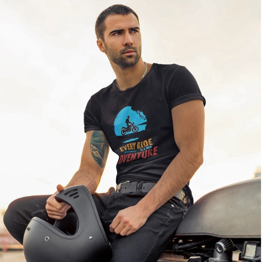 Man wearing a black t-shirt with a graphic design, holding a helmet, sitting on a motorcycle.